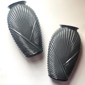 Könnte beinhalten: Zwei graue Vasen im Art-Deco-Stil mit einem fächerartigen Design. Die Vasen haben einen dunkelgrauen Rand und eine strukturierte Oberfläche. Die Vasen werden auf weißem Hintergrund präsentiert. Diese dekorativen Vasen sind perfekt, um jedem Raum einen Hauch von Vintage-Flair zu verleihen.
