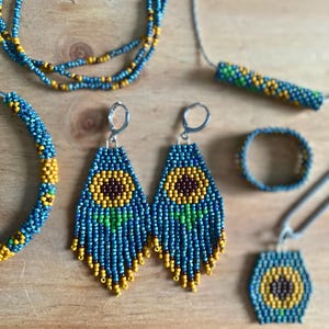 May include: A set of sunflower-themed jewelry, including a necklace, earrings, bracelet, and pendant. The jewelry is made with blue, yellow, and green beads.