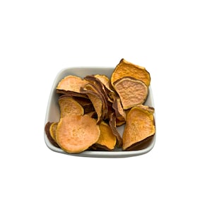 May include: A white ceramic bowl filled with sweet potato crisps. The crisps are a light orange colour and have a slightly crispy texture.