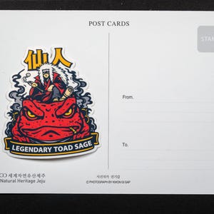 Puede incluir: Una postal con una pegatina de un personaje fumando en pipa, encima de un sapo rojo con el texto "LEGENDARY TOAD SAGE". La postal tiene l&iacute;neas para "De" y "Para", y el texto "POST CARDS".