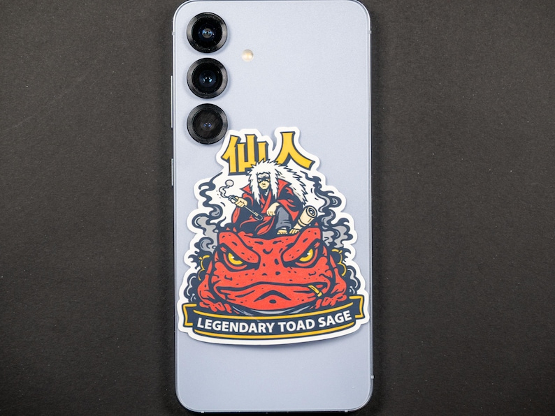 Puede incluir: Una pegatina con una ilustraci&oacute;n de dibujos animados de un personaje con cabello blanco y una t&uacute;nica roja, fumando un cigarrillo, sentado sobre un sapo rojo. El texto "Legendary Toad Sage" est&aacute; en una pancarta debajo.