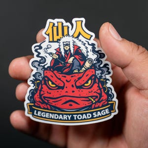 Puede incluir: Una pegatina con una ilustraci&oacute;n de dibujos animados de un personaje con cabello blanco y una t&uacute;nica roja, sentado sobre un sapo rojo. La pegatina tiene el texto "Legendary Toad Sage" y caracteres japoneses.
