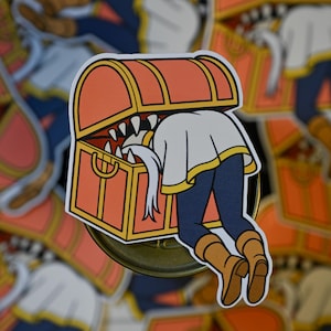 May include: A sticker featuring a cartoon illustration of a treasure chest with a person's legs and torso inside. The chest is orange with yellow trim and sharp teeth. The person wears a white shirt, blue pants, and brown boots.