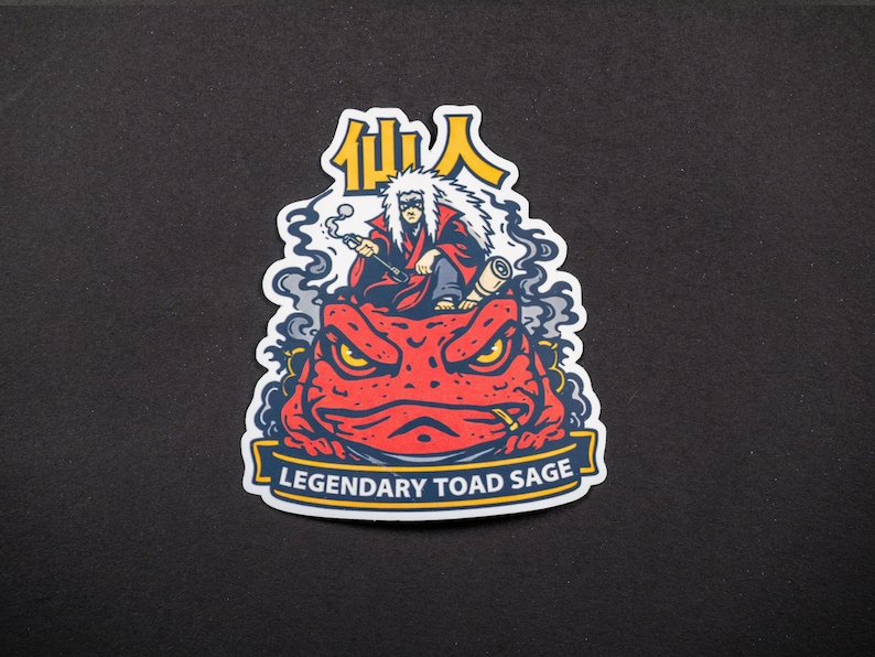 Puede incluir: Una pegatina con una ilustraci&oacute;n de dibujos animados de una figura con pelo blanco y una t&uacute;nica roja, fumando en pipa, sentado sobre un gran sapo rojo. El texto "Legendary Toad Sage" est&aacute; en una pancarta, con caracteres japoneses encima.