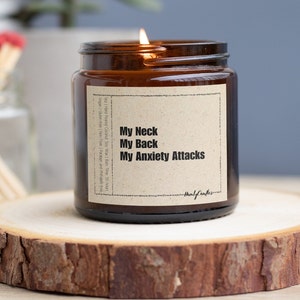 May include: A brown glass candle jar with a white label that reads "My Neck My Back My Anxiety Attacks". The candle is lit and the label also includes information about the candle, such as the burn time and ingredients.
