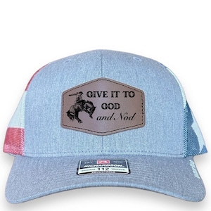 May include: A gray and blue trucker hat with a red, white, and blue American flag design on the side. The hat has a brown leather patch with the text "GIVE IT TO GOD and Nod" and a cowboy riding a bucking bronco.