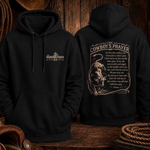 May include: A black hooded sweatshirt featuring a graphic on the front chest with the text Narrow Road and a bull illustration. The back displays a large graphic of a bull with the text The Cowboy's Prayer and a religious poem in tan ink.