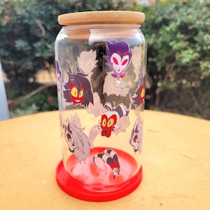 May include: A clear glass tumbler with a bamboo lid and a red base. The glass is decorated with cartoon character decals. The tumbler is designed to hold beverages and is suitable for both hot and cold drinks.