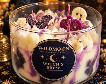 May include: A clear glass jar candle with a label reading WILDMOON CANDLES WITCH'S BREW. The wax is white and purple with piped white wax toppings shaped like a bat, a skull, and a pumpkin, all dusted with fine glitter and featuring multiple wicks.