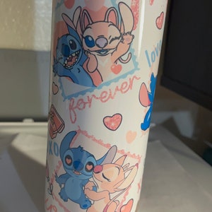 May include: A cylindrical tumbler with a white base featuring a pink glitter drip effect at the top. The design includes illustrations of blue and pink alien characters, red hearts, and the text "forever" and "XOXO" printed in a cursive pink font.