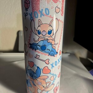 May include: A white cylindrical tumbler featuring a pink glitter drip design at the top. The surface is decorated with blue and pink cartoon characters, the text XOXO, pink hearts, a rose, and a key. The characters are shown in two separate frames.