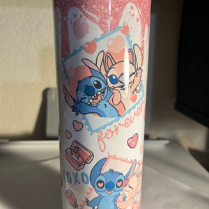 May include: A cylindrical tumbler featuring a pink glitter drip design at the top. The white surface displays cartoon characters Stitch and Angel in various poses, surrounded by pink hearts, the text forever, and XOXO, plus a small ring box graphic.