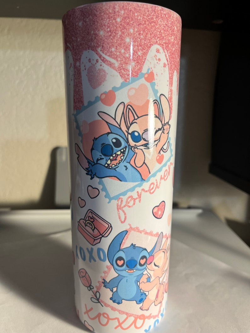 May include: A cylindrical tumbler featuring a pink glitter drip design at the top. The white surface displays cartoon characters Stitch and Angel in various poses, surrounded by pink hearts, the text forever, and XOXO, plus a small ring box graphic.