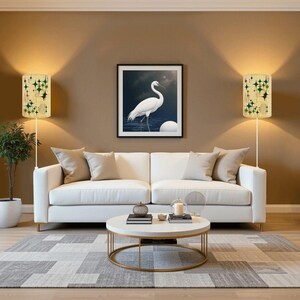 May include: A living room scene featuring a white sofa, a round coffee table, and a framed artwork of a white bird. Two wall lamps with green and gold starburst patterns flank the artwork. A gray and white geometric rug completes the decor.