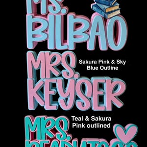Puede incluir: Letreros personalizados en tres dimensiones con el texto MS. BILBAO en azul cielo y rosa con un icono de libro, MRS. KEYSER en rosa con borde azul cielo, y MRS. READYTOGO en verde azulado con borde rosa y un icono de coraz&oacute;n rosa sobre fondo negro.