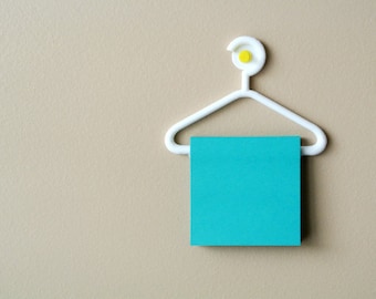 May include: A white plastic hanger with a yellow button on the top, holding a turquoise blue sticky note.