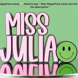Puede incluir: Un letrero tridimensional con el texto MISS JULIA en letras de color rosa claro con bordes gris oscuro, acompa&ntilde;ado de un emoji de cara feliz de color verde brillante con ojos y boca negros, todo sobre una superficie reflectante.