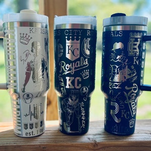 May include: Three stainless steel travel mugs with black and silver designs featuring the Kansas City Royals logo and team graphics. The mugs have handles and lids.
