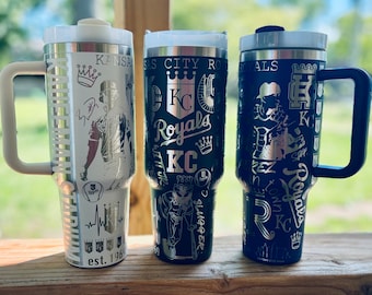 May include: Three stainless steel travel mugs with black and silver designs featuring the Kansas City Royals logo and team graphics. The mugs have handles and lids.