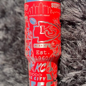 May include: Red stainless steel tumbler with a silver design featuring the Kansas City Chiefs logo, the team's name, and the city skyline. The text "Est. 1960" is also included in the design.