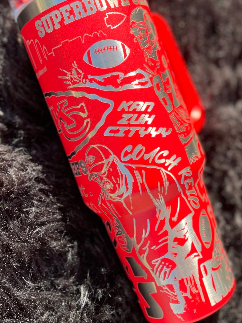 May include: Red stainless steel tumbler with a silver design featuring a football player, a football, and the text "SUPERBOWL", "KAN ZUH CITY", and "COACH".