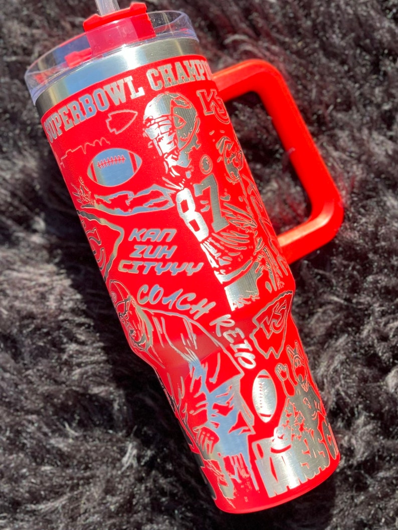 May include: Red stainless steel tumbler with a silver design featuring a football player, the words "Superbowl Champ", "Kan City", "Coach Reid", and "87".