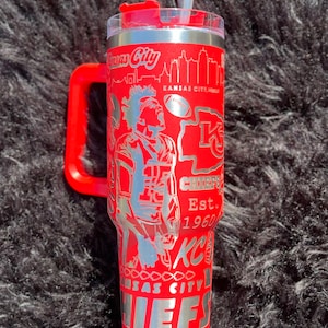 May include: Red stainless steel tumbler with a handle. The tumbler has a silver design featuring a football player, the Kansas City Chiefs logo, and the text "Kansas City Chiefs Est. 1960".
