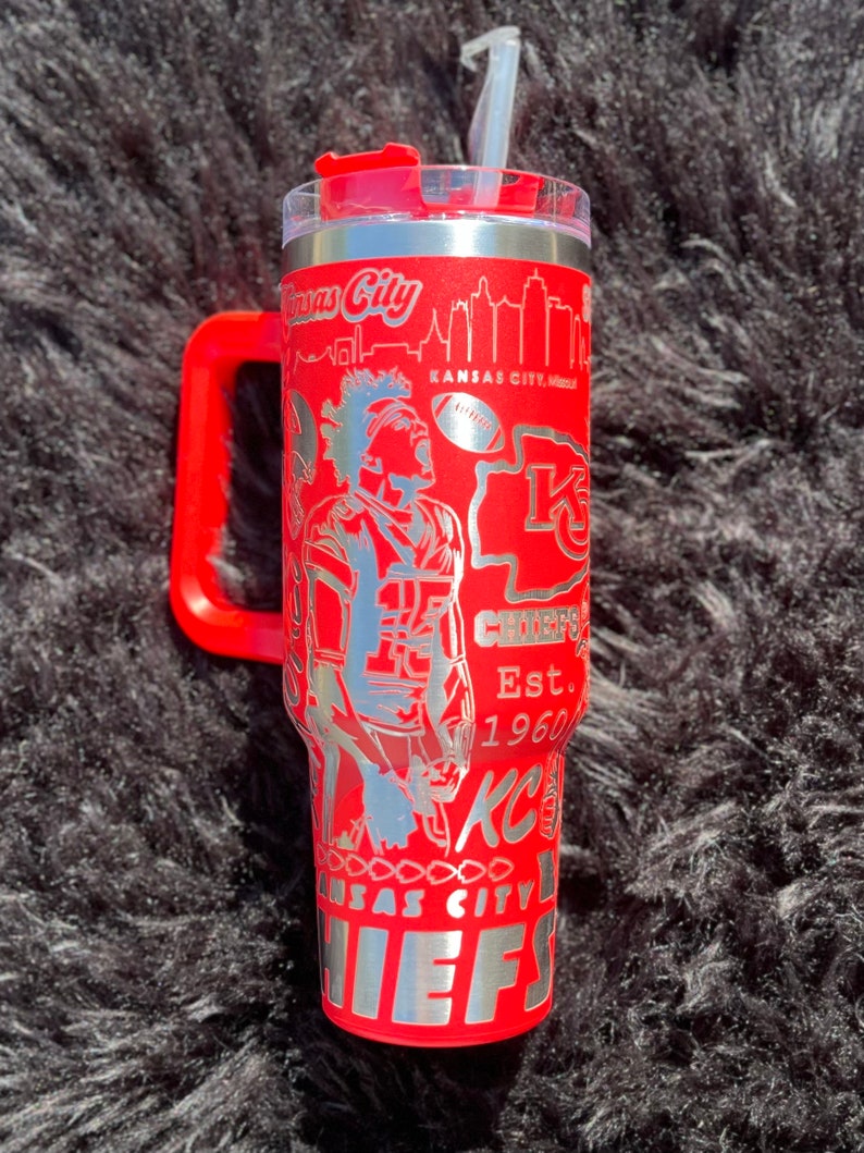 May include: Red stainless steel tumbler with a handle. The tumbler has a silver design featuring a football player, the Kansas City Chiefs logo, and the text "Kansas City Chiefs Est. 1960".