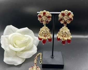 May include: Gold-toned jewelry set featuring earrings and a headpiece. The earrings have a floral design with red and clear stones, and dangling red beads. The headpiece mirrors the earring design, with a chain for securing.