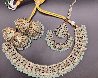 May include: A gold-toned jewelry set featuring a necklace, earrings, and a headpiece. The set is adorned with light green teardrop-shaped stones and small, round beads. The necklace and earrings have intricate designs.