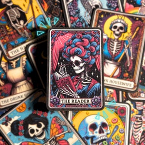 Könnte beinhalten: Eine Tarotkarte mit einem schwarz-weißen Skelett, das eine rosa-blaue Perücke trägt und ein Buch liest. Die Karte trägt den Titel "The Reader".