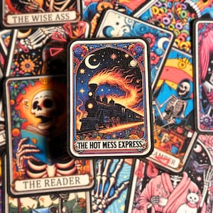 May include: A black and white tarot card with a dark blue background. The card features a train with a fiery plume of smoke, traveling through a starry night sky. The card is titled "The Hot Mess Express".