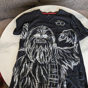 May include: Black t-shirt featuring a silver graphic of Chewbacca from Star Wars. The shirt has the text "Disney 100 Years of Wonder" on the front.