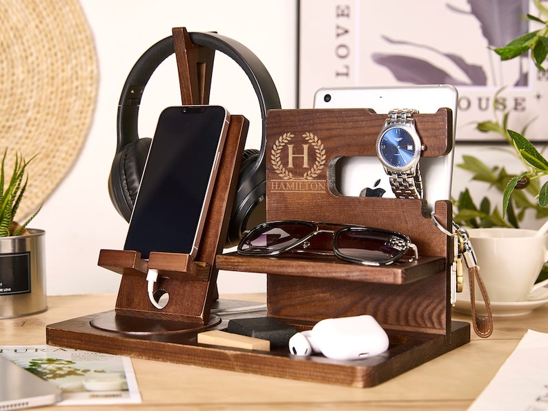 May include: A wooden organizer with a phone stand, headphone holder, watch stand, and a small shelf for glasses or other items. The organizer is personalized with the name "Hamilton" and a monogram "H".