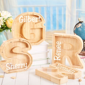 Puede incluir: Cuatro alcanc&iacute;as de madera con forma de las letras S, R, G y N. Las alcanc&iacute;as tienen ventanas de pl&aacute;stico transparente y est&aacute;n personalizadas con los nombres Sherry, Renee, Gilbert y Norman.