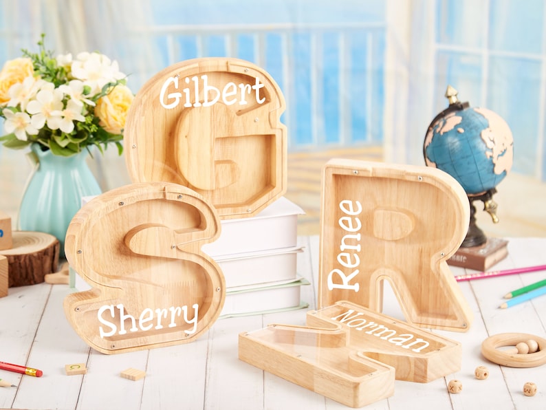 Puede incluir: Cuatro alcanc&iacute;as de madera con forma de las letras S, R, G y N. Las alcanc&iacute;as tienen ventanas de pl&aacute;stico transparente y est&aacute;n personalizadas con los nombres Sherry, Renee, Gilbert y Norman.