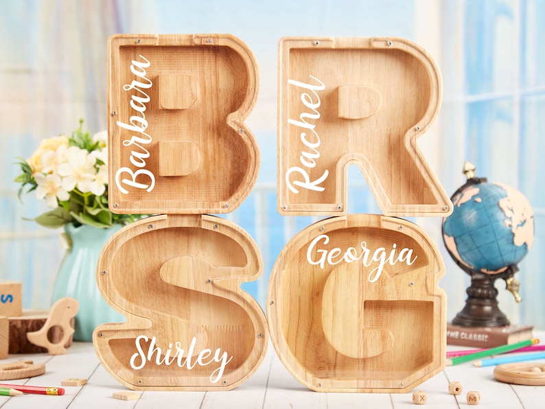 Puede incluir: Cuatro alcanc&iacute;as de madera con forma de las letras B, R, S y G. Cada alcanc&iacute;a tiene un nombre: Barbara, Rachel, Shirley y Georgia.