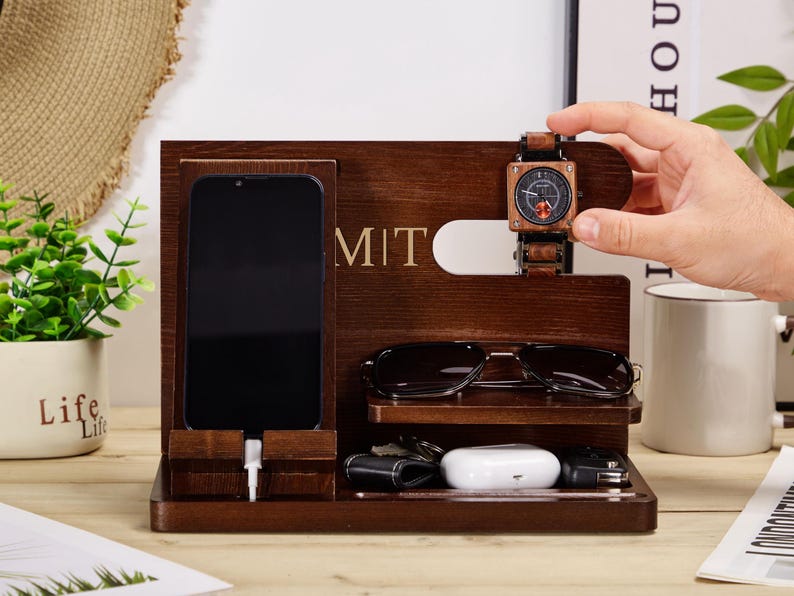 May include: A wooden organiser with compartments for a phone, watch, glasses, and other accessories. The organiser has the word "MIT" engraved on the front.