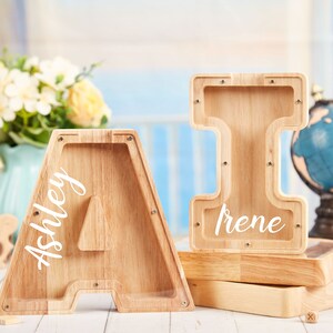 Puede incluir: Dos alcanc&iacute;as de madera con forma de letras, una es la letra A con el nombre Ashley escrito en ella, la otra es la letra I con el nombre Irene escrito en ella.