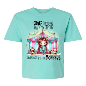 May include: A turquoise t-shirt with a cartoon illustration of a girl standing in front of a pink and white striped circus tent. The text on the shirt reads "CRAP. Turns out this is my circus and those are my MONKEYS."