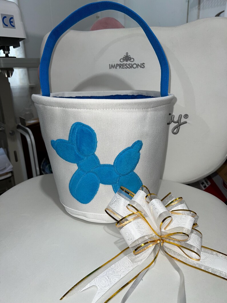 Personalized with buyers choice of name. White canvas Easter Basket with Blue Balloon Dog applique, includes tissue paper, bow and clear gift wrapper. Personalization in blue
