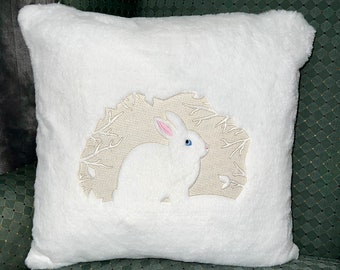 May include: White faux fur pillow with an embroidered design of a white rabbit in a forest setting.