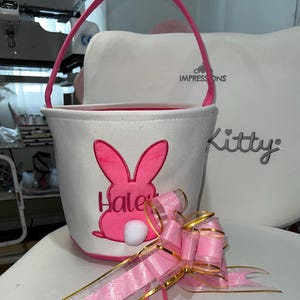 Personalized with buyers choice of name. White canvas Easter Basket with Pink Bunny applique, includes tissue paper, bow and clear gift wrapper