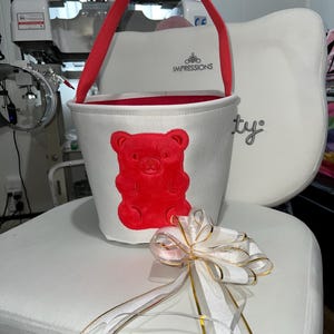 Personalized with buyers choice of name. White canvas Easter Basket with Berry Gummy Bear applique, includes tissue paper, bow and clear gift wrapper