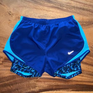 May include: Blue running shorts with a white Nike swoosh logo and a blue and black patterned liner.
