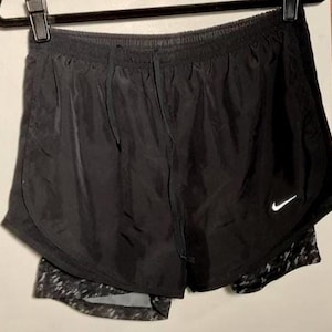 May include: Black running shorts with a built-in liner. The shorts have a white Nike swoosh logo on the right leg.