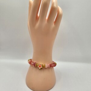 Crystal bracelet made of strawberry quartz, peach rice topaz, watermelon quartz and red chalcedony with gold flower and ball spacers and large gold sakura flower charm detailed with pink enamel.
