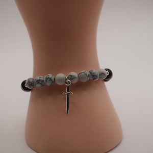 May include: A white and black marbled bead bracelet with a silver cross charm.