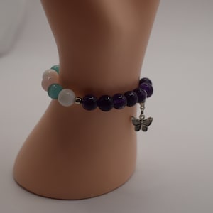 May include: A purple amethyst gemstone bracelet with a butterfly charm. The bracelet has white and light blue beads.