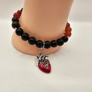May include: A black and red beaded bracelet with a silver heart charm. The heart charm has a red enamel finish.